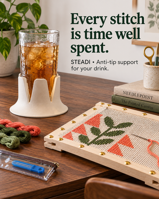 White Steadi supporting an iced-tea glass beside a needlepoint frame and skeins of thread on a wooden table. Illustrative AI-generated scene.
