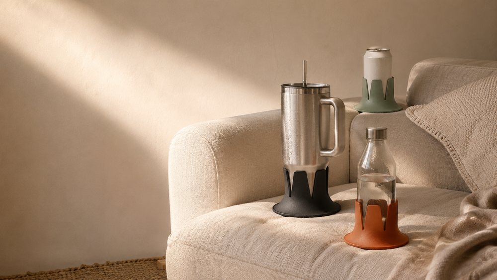 A tumbler and a can, each wearing a Steadi, stand upright on a couch.